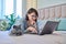 Woman together with cat lying on bed at home, female using laptop