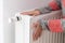 A woman touches a cold radiator of a home heater and increases the heating power