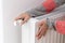 A woman touches a cold radiator of a home heater and increases the heating power