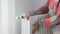 A woman touches a cold radiator of a home heater and increases the heating power