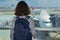 Woman tourist in airport terminal waiting for flight and looking at airplane