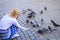 Woman tourist or citizen toss crumbs for pigeons. Girl blonde woman relaxing city square and feeding pigeons. Girl
