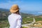 Woman in tourist clothes and straw hat standing on top of a mountain.