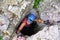 Woman tourist exiting a cave through very narrow opening, wearing via ferrata gear. Location: Baia de Fier, Romania