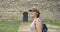 Woman tourist in hat with backpack walking in the park near ancient medieval castle