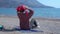 Woman tourist puts on red bandana resting on empty sandy beach near tranquil azure sea on sunny spring day backside view