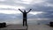 A woman tourist raises her hands up, standing on a pier above the sea against the background of the sky and mountains