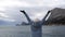A woman tourist raises her hands up, standing on a pier over the sea against the background of the sky and mountains