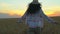 Woman tourist running in wheat field at summer sunset. Hiker traveler woman in hat with backpack hikking in nature. Girl