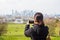 Woman tourist taking pictures in the park with city bulding in background.