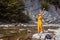 Woman tourist walking by mountain river enjoying landscape. Traveler feels happy raising arms. Summer vacation