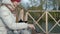 Woman tourist in warm clothes on the bridge by the river bank with a backpack, preparing sausages on the grill, picnic