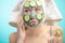 Woman with towel on head and face mask enriching with cucumbers via smartphone