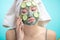 Woman with towel on head and face mask enriching with cucumbers via smartphone