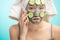 Woman with towel on head and face mask enriching with cucumbers via smartphone