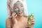 Woman with towel on head and face mask enriching with cucumbers via smartphone