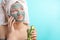 Woman with towel on head and face mask enriching with cucumbers via smartphone