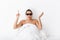 Woman with towel on head lies in bed covering body under blanket isolated over white wall background wearing sunglasses pointing