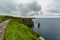 Woman on a trail admiring the landscape on the Cliffs of Moher from a hill