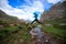 Woman trail runner jumping over stream water at mountain