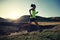 Woman trail runner running in sunset grassland