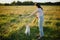 Woman training cute white puppy to behave in summer meadow in warm sunset light. Adorable fluffy puppy looking at girl owner for a