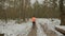 Woman training in park. Confident female athlete in blue leggins and orange jacket running in winter forest, back side follow view