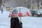 A woman with a transparent umbrella crosses the road. Blizzard.
