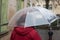 Woman with transparent umbrella and red coat walking in cobbles street