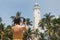 Woman traveler in dress in front of famous landmark of Sri Lanka country taking photo on smartphone of Dondra lighthouse