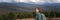 Woman traveler with gray backpack standing on background of mountain landscape on cold foggy cloudy day