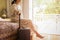 Woman traveler with luggage sitting on the bed in hotel room with garden view.