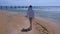 Woman traveller walks on shells, sea water and sand on the beach wearing in hat.