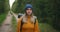 A woman travels on foot in a sweater and hat along a forest road with a backpack and examines the trees and nature