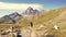 Woman trekking in idyllic mountain landscape on footpath crossing blooming green meadow set amid high altitude rocky mountain