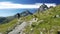 Woman trekking in idyllic mountain landscape on footpath crossing blooming green meadow set amid high altitude rocky mountain rang