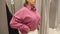 A woman tries on a pink shirt in a women's clothing store.