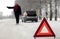 A woman tries to stop a car on a winter road. Sign on an emergency stop.