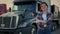 A woman trucker stands in front of a black semi truck