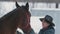 Woman is trying leads stubborn horse to walking in snowy paddock during snowfall