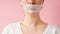 A woman turns and shows her mouth taped shut. Close up. Pink background. Concept of secrets and female's rights