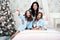 Woman with two children in blue knit cardigan in the bed near Christmas tree