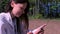 Woman is typing message on smartphone sitting on nature, side view.