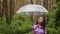 A woman with an umbrella in her hand in the rain. A girl in a purple shirt under an umbrella in the woods. A woman with