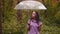 A woman with an umbrella in her hand in the rain. A girl in a purple shirt under an umbrella in the woods. A woman with