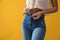 Woman unbuttoning jeans on yellow background