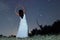 Woman under starry night in white long dress ballet pose raising arms Woman under night sky