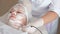 A woman undergoes ultrasonic phonophoresis of skin lifting at a cosmetology clinic. The hands of a beautician smooth out