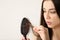 Woman untangling her hair from brush on light background.