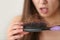 Woman untangling her hair from brush on light background